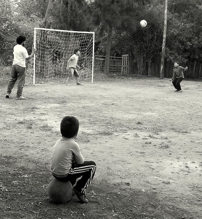 Niño sentado sobre una pelota aguardando que lo inviten a jugar dentro de la cancha